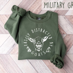 May include: A military green sweatshirt with the text "Easily Distracted by Goats" in white lettering and a white goat illustration.