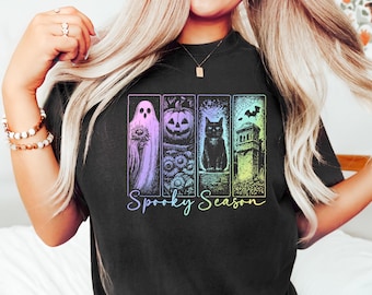 Puede incluir: Camiseta negra con un gráfico colorido que presenta un fantasma, una calabaza, un gato negro y una torre. Las palabras "Spooky Season" están escritas en una fuente degradada debajo de las imágenes. La camiseta es de estilo casual y cómodo.