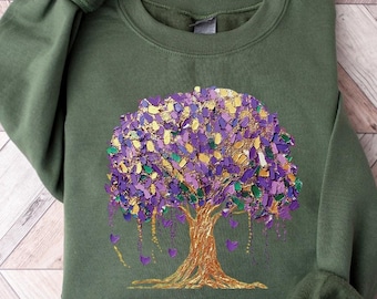 May include: A green sweatshirt with a gold and purple tree design. The tree is made of small, colorful pieces that resemble confetti.