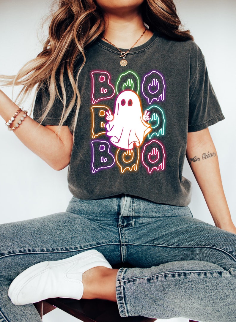 Puede incluir: Una camiseta gris oscuro con un gr&aacute;fico de ne&oacute;n de un fantasma con la palabra "BOO" escrita en letras de ne&oacute;n que gotean.