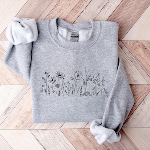 May include: A gray sweatshirt with a black floral design on the front. The design features a row of small flowers and leaves.