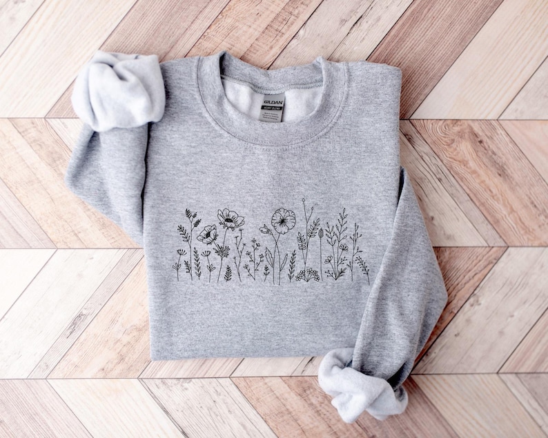 May include: A gray sweatshirt with a black floral design on the front. The design features a row of small flowers and leaves.