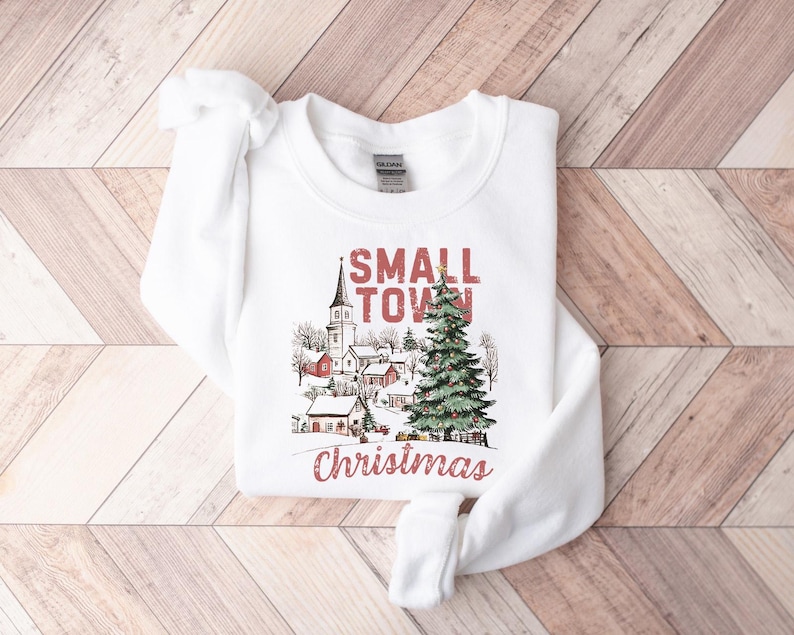 May include: White sweatshirt with a red and black graphic design that says "Small Town Christmas". The graphic features a church, houses, and a Christmas tree.