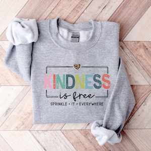 May include: Gray sweatshirt with the text "KINDNESS is free" in rainbow colors and a small leopard print heart. The text below says "SPRINKLE IT EVERYWHERE".