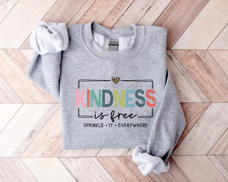 May include: Gray sweatshirt with the text "KINDNESS is free" in rainbow colors and a small leopard print heart. The text below says "SPRINKLE IT EVERYWHERE".