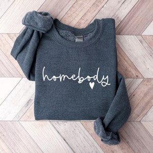 May include: A dark gray sweatshirt with the text "homebody" in white lettering and a small white heart.