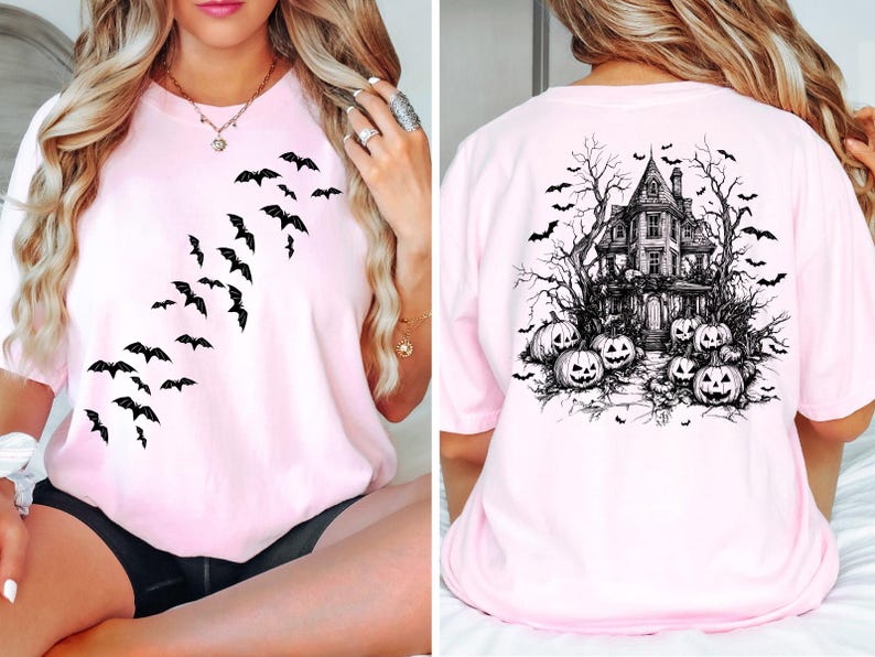 Op de afbeelding: Roze T-shirt met een zwart vleermuisontwerp aan de voorkant en een zwart spookhuis- en pompoenontwerp aan de achterkant.