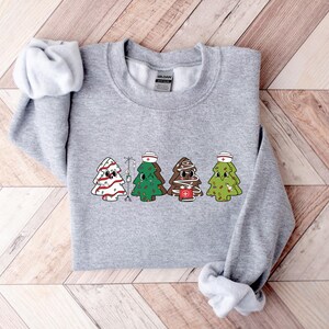 May include: A gray sweatshirt with a Christmas tree design. The trees are wearing nurse hats and have IV bags. The text "HOLIDAY" is on the tag.