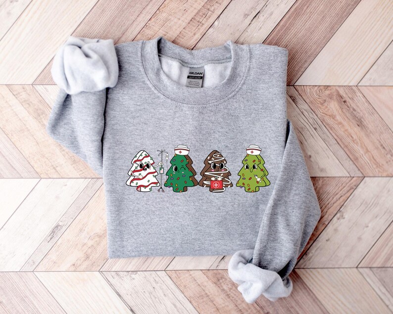 May include: A gray sweatshirt with a Christmas tree design. The trees are wearing nurse hats and have IV bags. The text "HOLIDAY" is on the tag.