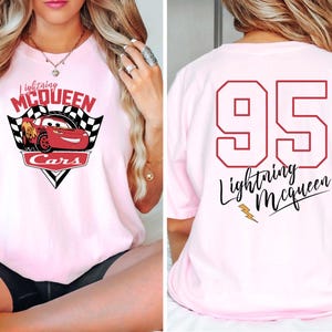 May include: Pink t-shirt featuring a red cartoon racing car with the text "Lightning McQueen Cars" on the front. The back of the shirt displays the number "95" and the text "Lightning McQueen" in a cursive font.