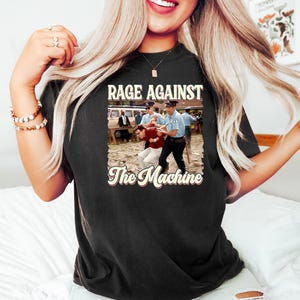 K&ouml;nnte beinhalten: Schwarzes T-Shirt mit einem Vintage-Grafikdruck der Band Rage Against The Machine. Die Grafik zeigt ein Schwarzwei&szlig;foto eines Mannes, der von Polizisten verhaftet wird.