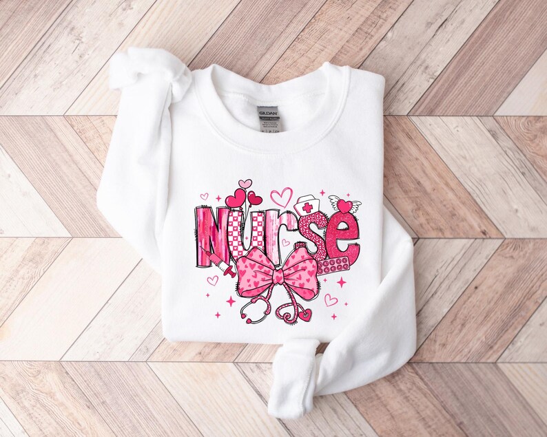 May include: White sweatshirt with a pink and white graphic design that says "Nurse" with hearts, a stethoscope, and a bandage.
