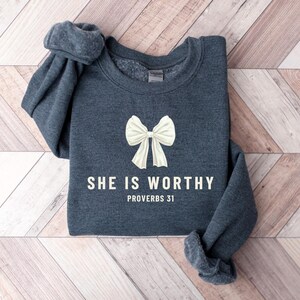 May include: A dark gray sweatshirt with a white bow and the text "She is worthy Proverbs 31" printed on the front.