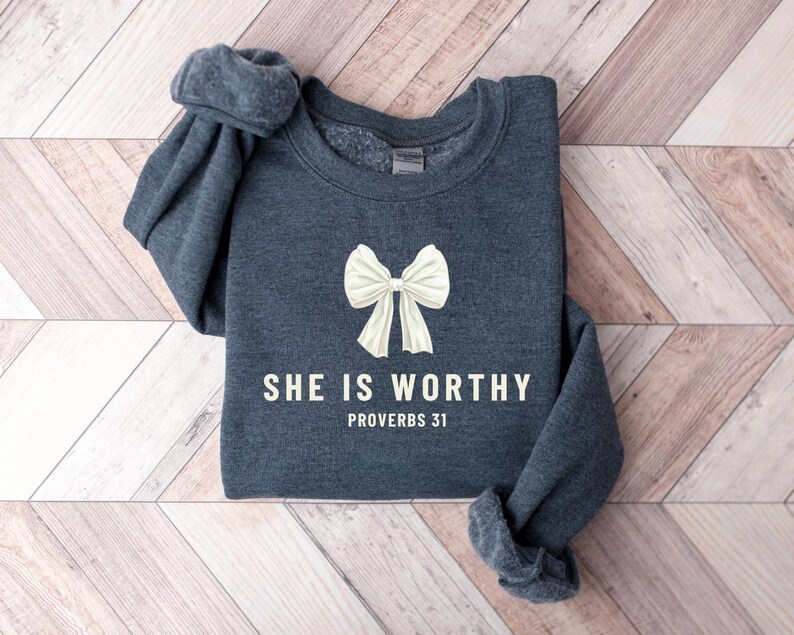 May include: A dark gray sweatshirt with a white bow and the text "She is worthy Proverbs 31" printed on the front.
