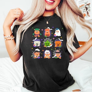 May include: Black t-shirt with a graphic print of nine cartoon characters dressed in Halloween costumes. The characters are holding candy buckets and are surrounded by candy corn, stars, and spiderwebs.