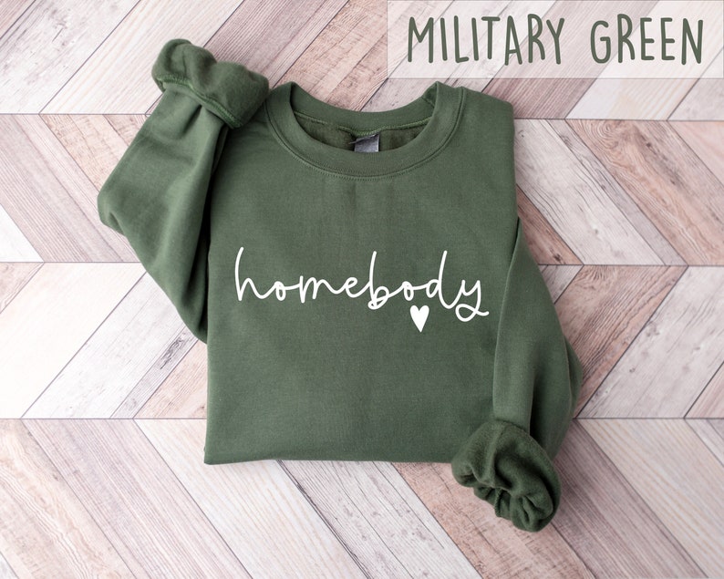 May include: A military green sweatshirt with the text "homebody" in white lettering and a small white heart.