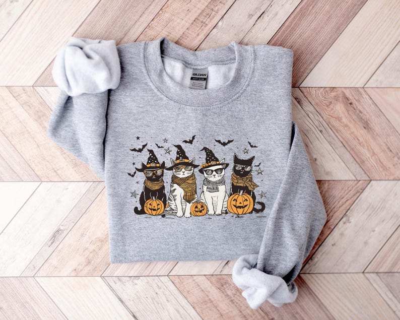 May include: A gray sweatshirt with a graphic of four cats wearing witch hats and holding pumpkins. The cats are wearing glasses and have different colored fur. The text "Hocus Pocus" is on one of the cats' hats.