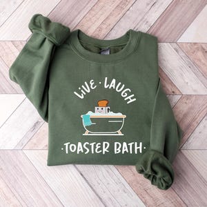 May include: Green sweatshirt with the text "Live Laugh Toaster Bath" and a cartoon illustration of a toaster in a bathtub.