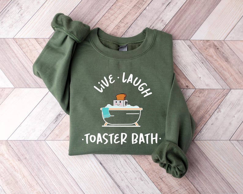 May include: Green sweatshirt with the text "Live Laugh Toaster Bath" and a cartoon illustration of a toaster in a bathtub.