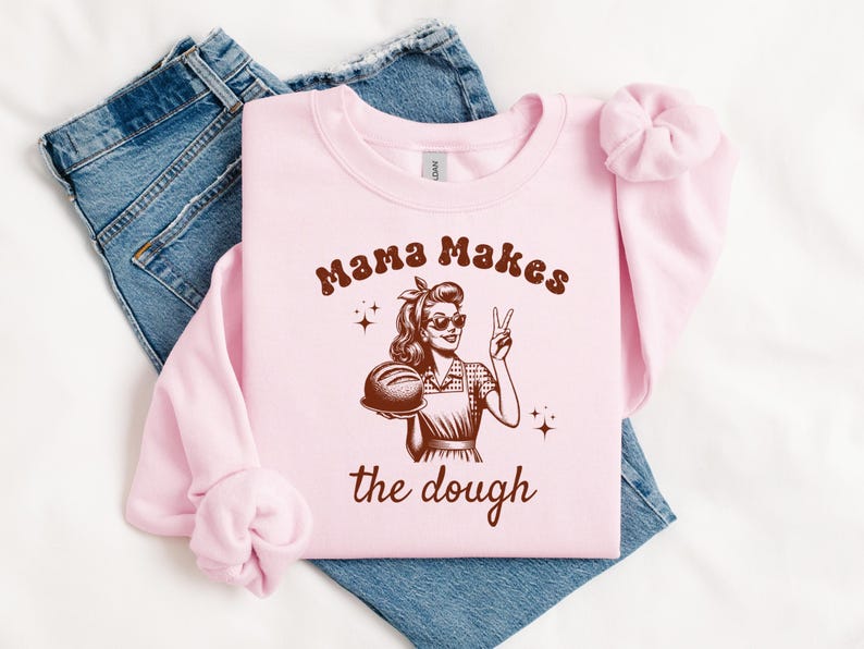 May include: Pink sweatshirt with a brown graphic of a woman holding a loaf of bread and the text "Mama Makes the Dough".