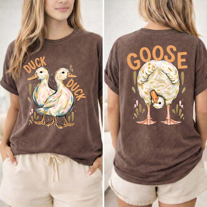 Puede incluir: Camiseta marr&oacute;n con un gr&aacute;fico de pato en la parte delantera y un gr&aacute;fico de ganso en la parte trasera. La parte delantera de la camiseta presenta dos patos con la palabra "DUCK" arriba y abajo. La parte trasera de la camiseta tiene un ganso con la palabra "GOOSE" arriba.