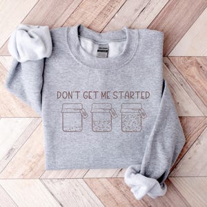 May include: Grey sweatshirt with the text "Don't get me started" and a graphic of three jars with lids.
