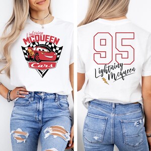 May include: White t-shirt with a red, yellow, and black Cars graphic on the front. The graphic features Lightning McQueen and the text "Lightning McQueen Cars". The back of the shirt has the number "95" in red with the text "Lightning McQueen" in black.