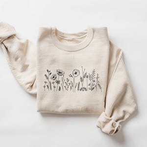 May include: A beige sweatshirt with a black line drawing of wildflowers on the front.