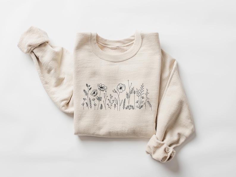 May include: A beige sweatshirt with a black line drawing of wildflowers on the front.
