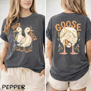 Puede incluir: Camiseta gris oscuro con un gr&aacute;fico de pato en la parte delantera y un gr&aacute;fico de ganso en la parte trasera. La parte delantera presenta dos patos con la palabra "DUCK" arriba y a un lado. La parte trasera tiene un ganso inclinado con la palabra "GOOSE" arriba.