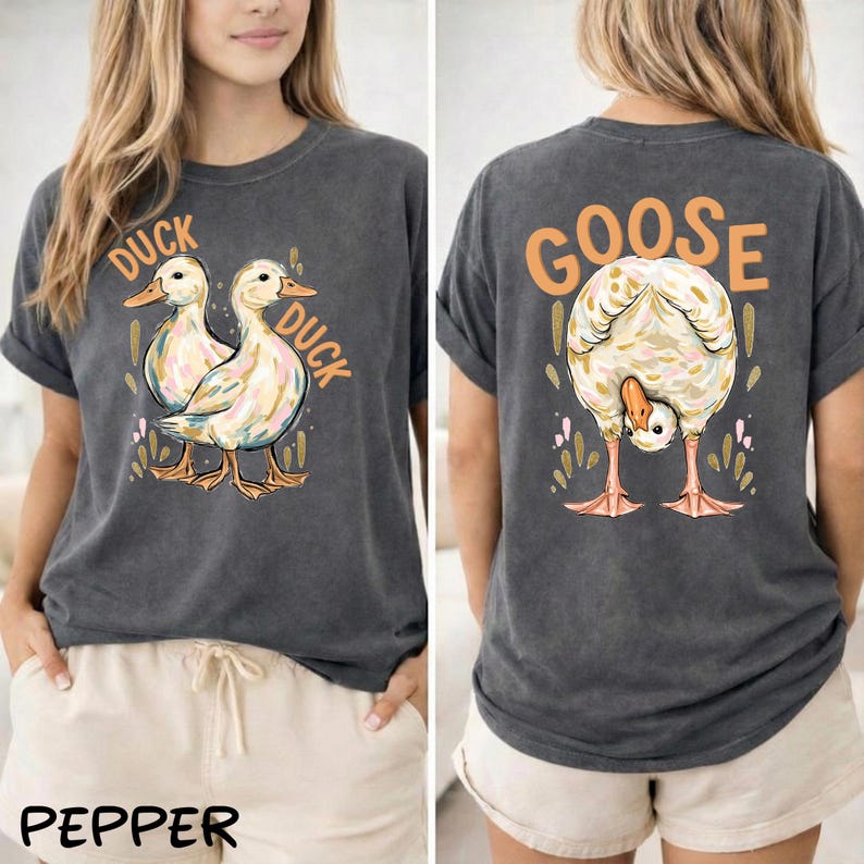 Puede incluir: Camiseta gris oscuro con un gr&aacute;fico de pato en la parte delantera y un gr&aacute;fico de ganso en la parte trasera. La parte delantera presenta dos patos con la palabra "DUCK" arriba y a un lado. La parte trasera tiene un ganso inclinado con la palabra "GOOSE" arriba.