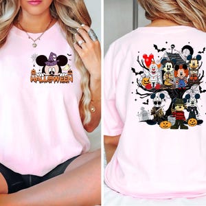 May include: Pink t-shirt with a Halloween theme featuring Mickey Mouse and other characters. The front of the shirt has a cartoon of Mickey Mouse with a witch's hat and the word "HALLOWEEN". The back of the shirt has a cartoon of Mickey Mouse and other characters in a spooky tree.