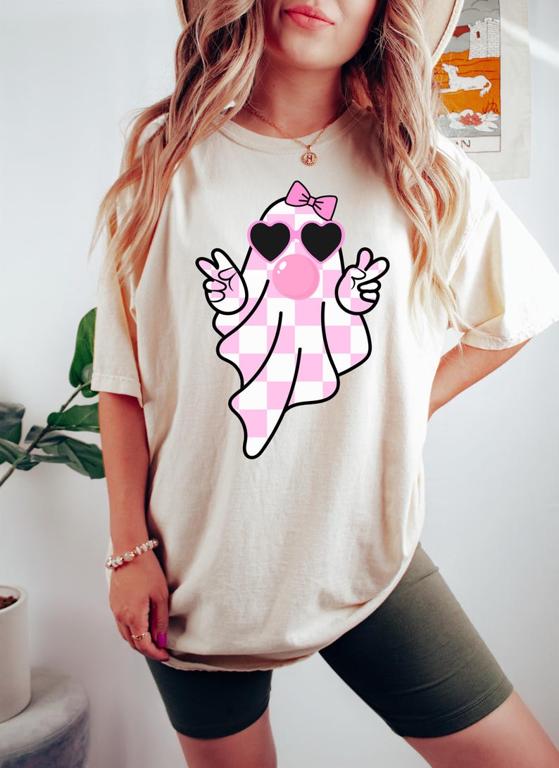 Peut inclure: Un t-shirt blanc avec un fant&ocirc;me &agrave; carreaux rose et blanc portant des lunettes de soleil en forme de c&oelig;ur rose et un n&oelig;ud rose. Le fant&ocirc;me souffle une bulle rose.