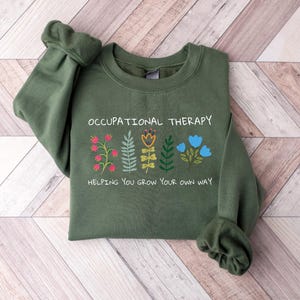 May include: A green sweatshirt with the text "Occupational Therapy" and a graphic of flowers with the text "Helping you grow your own way".