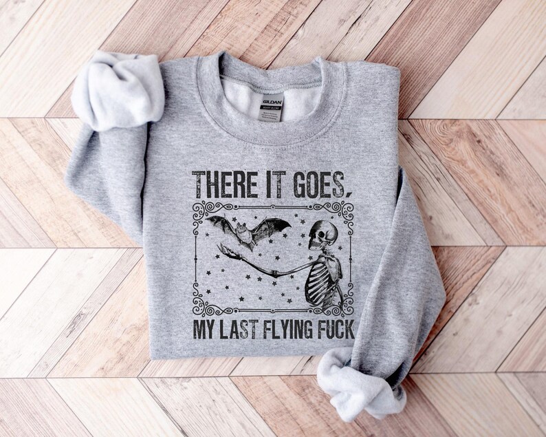 May include: Gray sweatshirt with a black and white graphic of a skeleton holding a bat with the text "There it goes, my last flying f***".