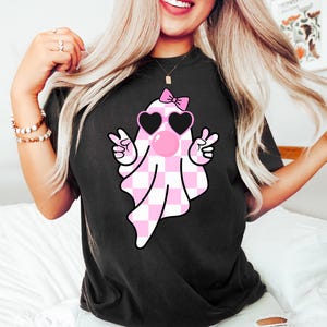 Peut inclure: T-shirt noir avec un fant&ocirc;me &agrave; carreaux rose et blanc portant des lunettes en forme de c&oelig;ur et un n&oelig;ud rose. Le fant&ocirc;me souffle une bulle rose.