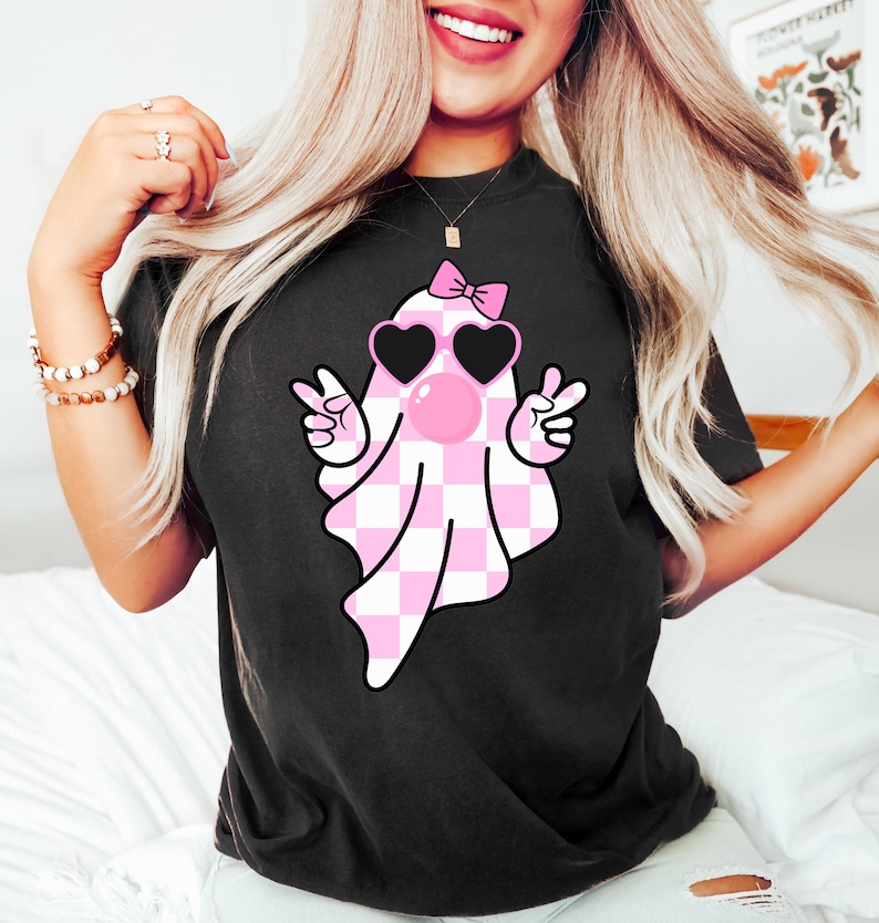 Peut inclure: T-shirt noir avec un fant&ocirc;me &agrave; carreaux rose et blanc portant des lunettes en forme de c&oelig;ur et un n&oelig;ud rose. Le fant&ocirc;me souffle une bulle rose.