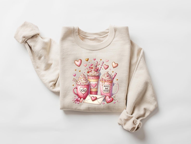 May include: Beige sweatshirt with a pink and white graphic of three mugs with whipped cream and hearts. The mugs say "XOXO" and "Hugs and Kisses".