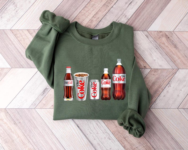 May include: A green sweatshirt featuring a graphic of four Coca-Cola products: a glass bottle of Coca-Cola, a can of Diet Coke, a can of Coca-Cola, and a glass bottle of Diet Coke.