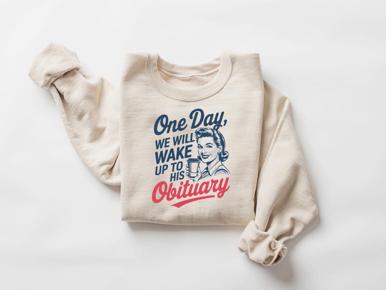 Puede incluir: Sudadera color crema con el texto "One Day, We Will Wake Up to His Obituary" en azul y rojo. Presenta una ilustraci&oacute;n de estilo vintage de una mujer sosteniendo una taza.