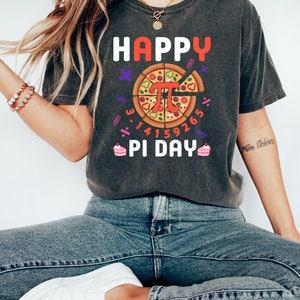 May include: A dark grey t-shirt with the text "HAPPY PI DAY" and a pizza slice with the mathematical symbol for pi in the center. The pizza slice is surrounded by the numbers 3.14159265.