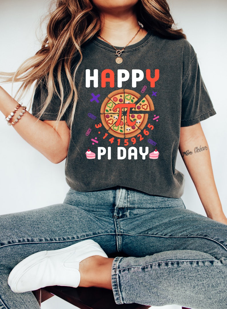 May include: A dark grey t-shirt with the text "HAPPY PI DAY" and a pizza slice with the mathematical symbol for pi in the center. The pizza slice is surrounded by the numbers 3.14159265.