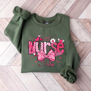 May include: Green sweatshirt with a pink and white graphic that says "Nurse" with hearts, a stethoscope, and a bandage.