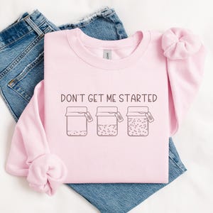 May include: Pink sweatshirt with the text "Don't get me started" and a graphic of three jars with lids. The jars are filled with different patterns.