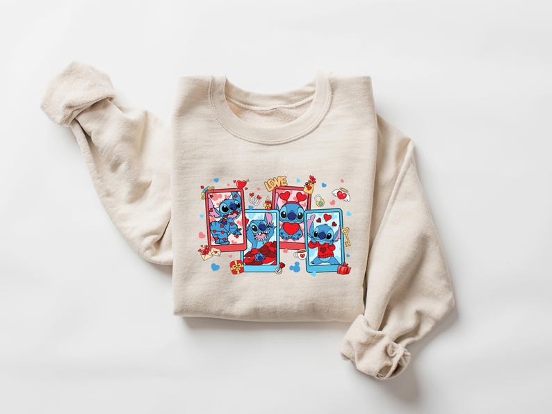 May include: A beige sweatshirt with a graphic print of Stitch from Lilo & Stitch. Stitch is shown in four different poses, each with a red heart and surrounded by hearts and other Valentine's Day themed graphics. The text "LOVE" is printed above the graphic.