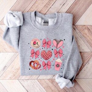 May include: Gray sweatshirt with a pink and white graphic design featuring a heart-shaped pastry, a heart-shaped taco, a coffee cup, and a bow. The graphic also includes the text "Marranito"