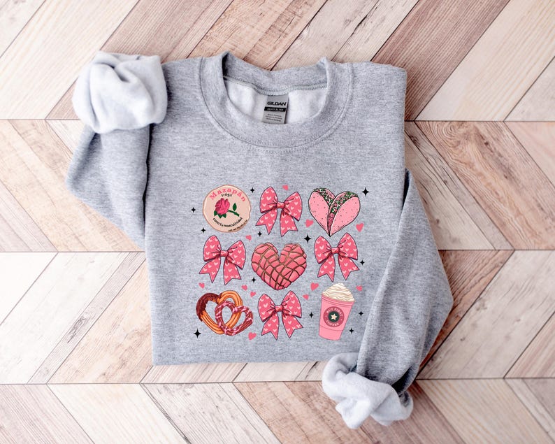 May include: Gray sweatshirt with a pink and white graphic design featuring a heart-shaped pastry, a heart-shaped taco, a coffee cup, and a bow. The graphic also includes the text "Marranito"
