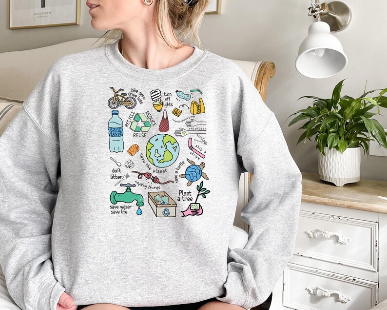 May include: A gray sweatshirt with a colorful graphic print of various environmental messages and illustrations. The graphic includes a bicycle, a water bottle, a turtle, a tree, and the words "Save the Planet", "Recycle", "Reduce", "Reuse", "Don't Litter", "Save Water Save Life", and "Plant a Tree".