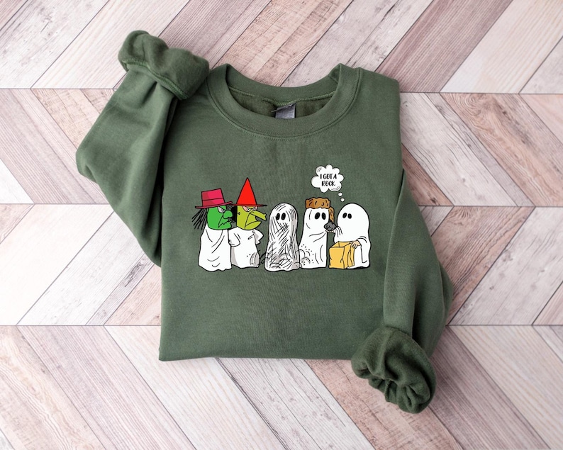 Puede incluir: Sudadera verde con un gr&aacute;fico de fantasmas y una bruja de la caricatura de Peanuts. El texto en la burbuja de pensamiento dice "Tengo una roca."