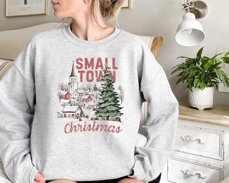 May include: A gray sweatshirt with a winter scene and the text "Small Town Christmas". The scene includes a church, houses, and a Christmas tree.